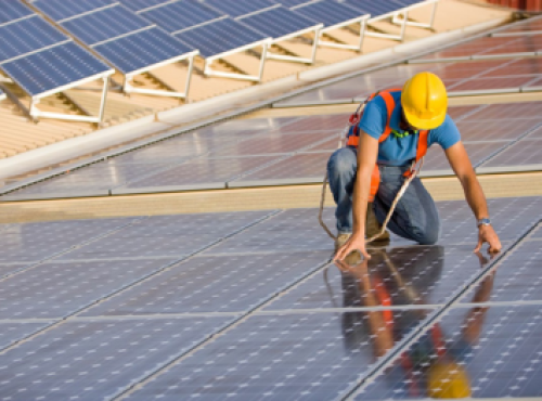 Photograph of a person wearing a hard hat installing solar PV panels. 