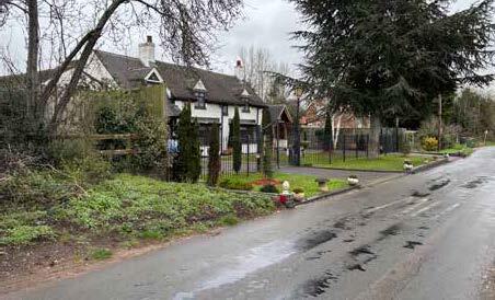 A suburban street scene featuring a house surrounded by trees and a garden.