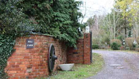 A brick wall with a sign that reads "Hill Farm," topped with greenery and an old-fashioned water wheel attached to the wall.