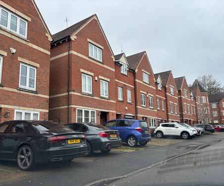 A photo of more modern townhouses reflecting local material palette and roofscape but front gardens dominated by parked vehicles